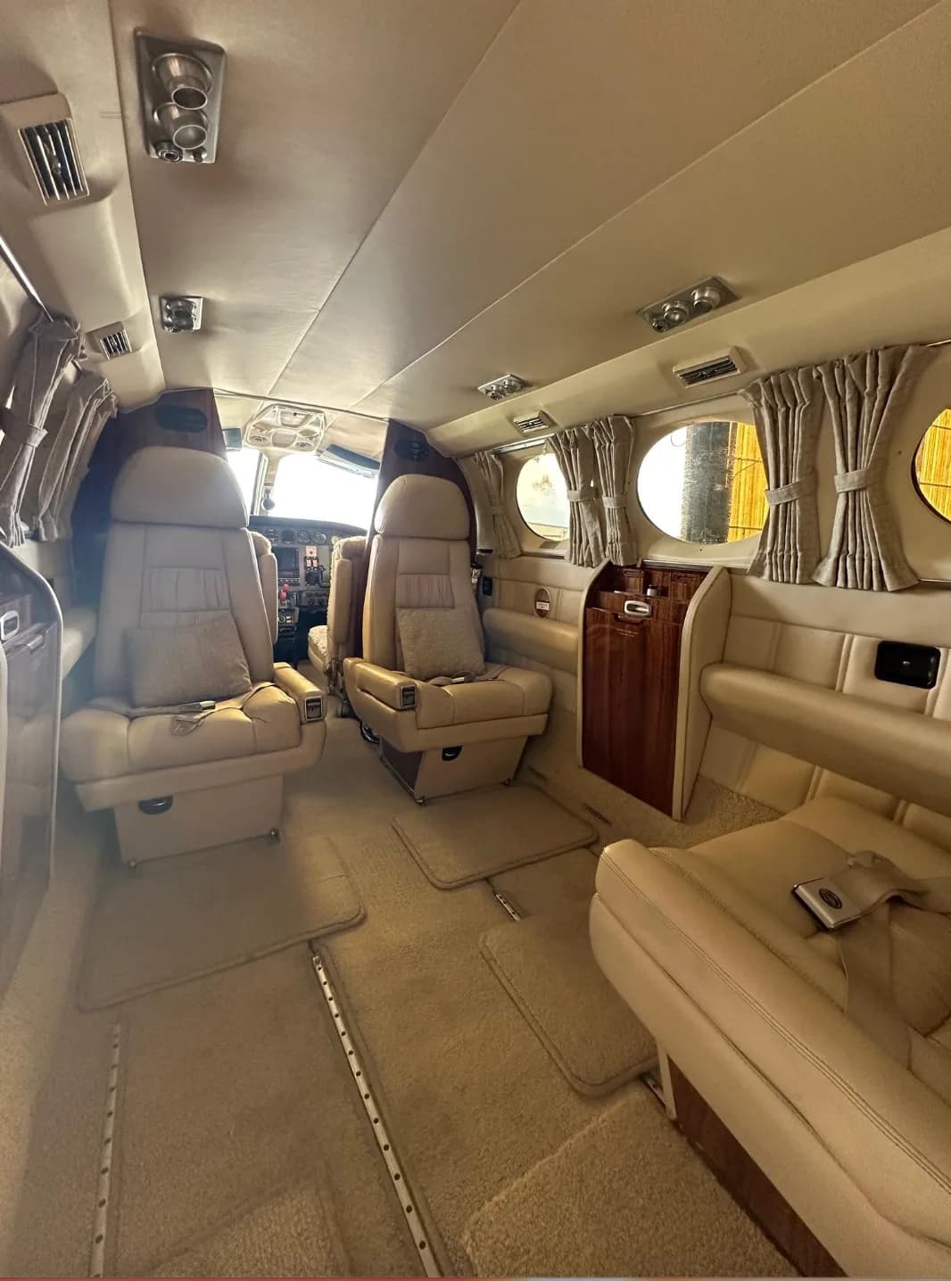 The spacious beige leather interior cabin of a private aircraft, looking towards the cockpit.