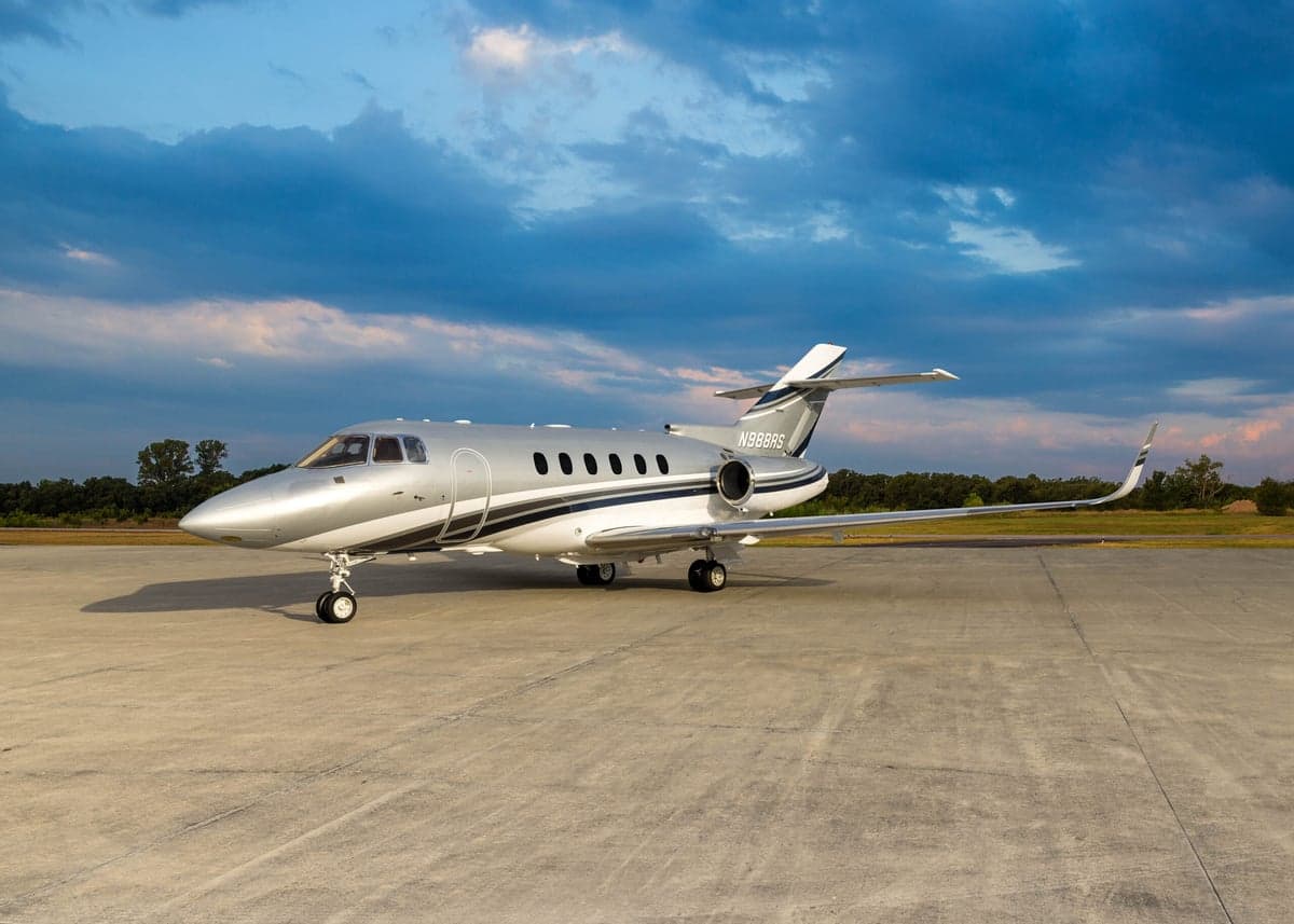 A silver and white Hawker 800XP aircraft, registration N988RS, is parked on the tarmac under a cloudy sky.