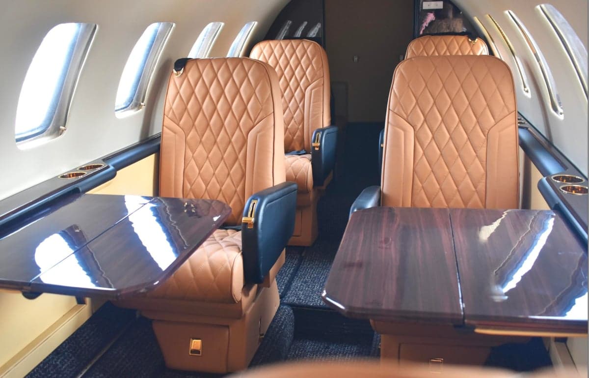 The interior of an aircraft with tan leather seats and dark wood tables.