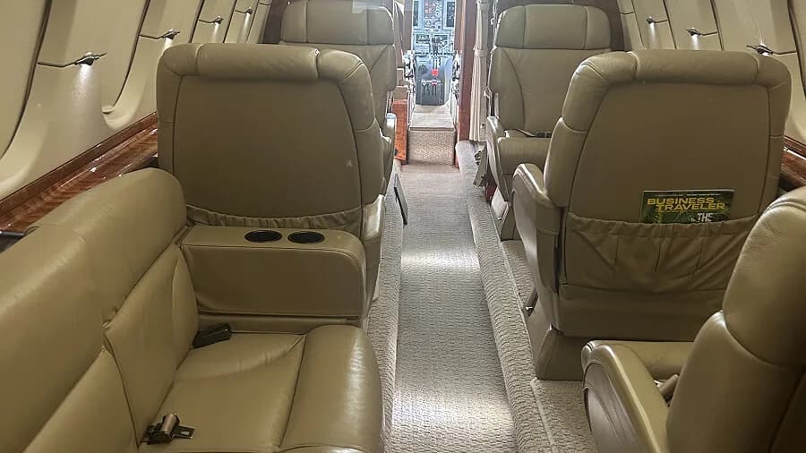 A view of the aircraft's interior cabin, showing beige leather seats and a magazine in a seat-back pocket.