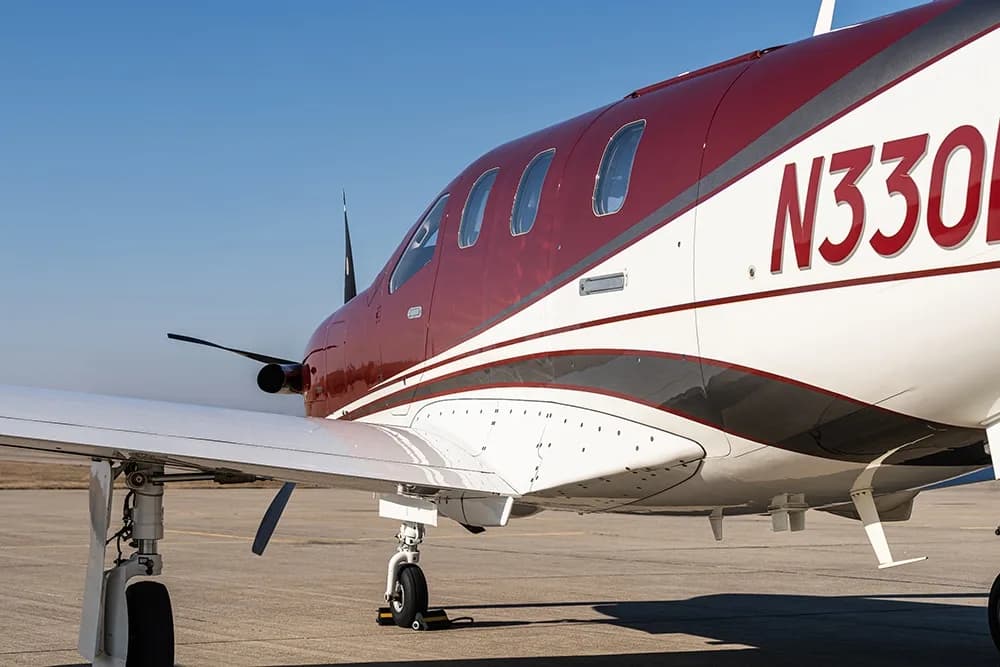 Side view of the fuselage of a maroon and white Daher TBM 900 aircraft, showing the registration N330EA.
