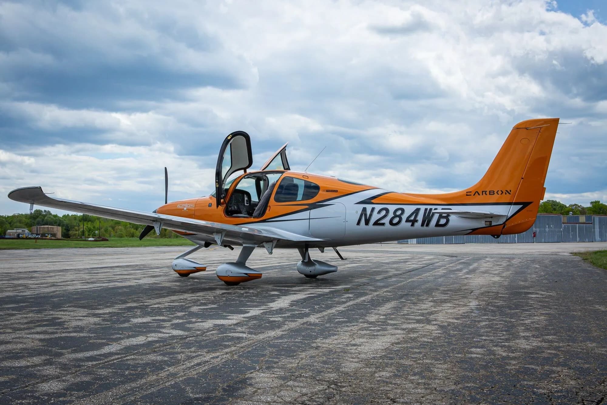 A side view of an orange and silver Cirrus SR20 aircraft, N284WB, with the pilot's door open on an airfield.