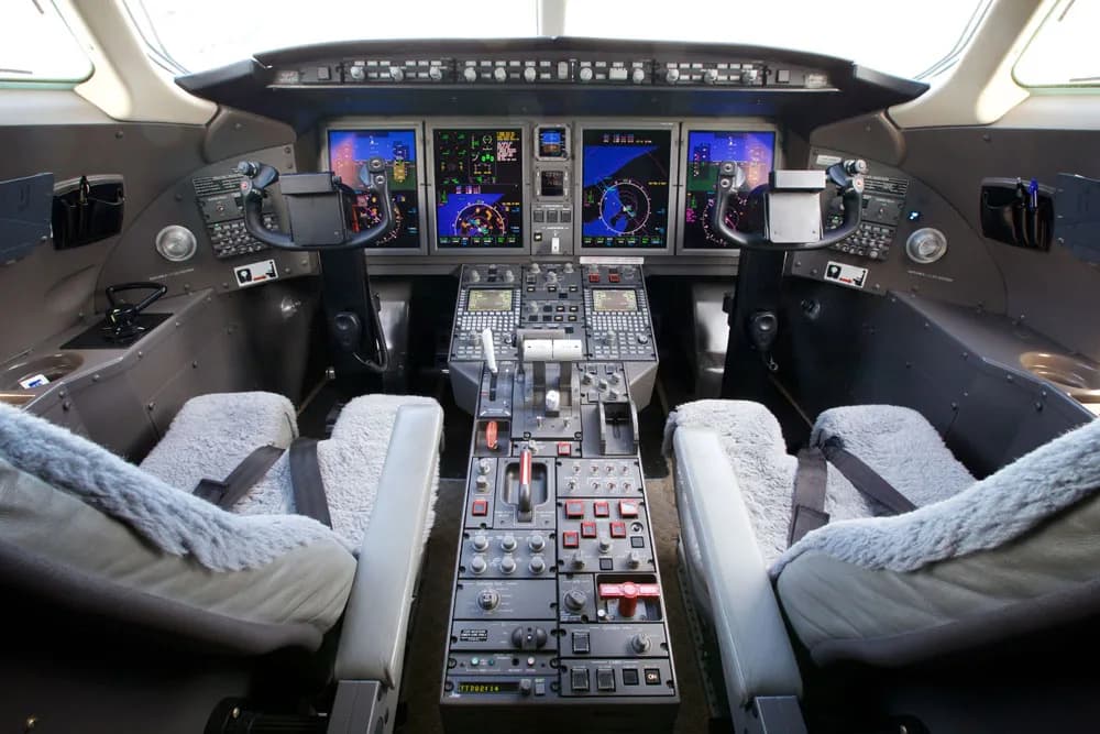 View down the aisle of the aircraft cabin with cream-colored leather seats and wood trim.