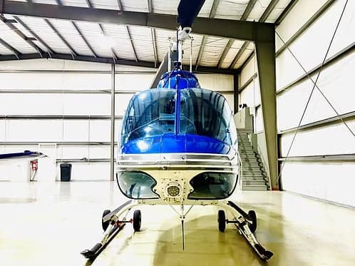 Front view of a blue and white Bell 407 helicopter parked in a hangar.