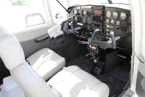 The cockpit of a Piper PA-28-181 Archer II features white seats and a black instrument panel.