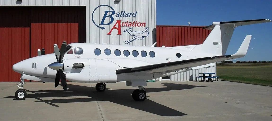 Side view of a white King Air aircraft parked in front of a hangar.