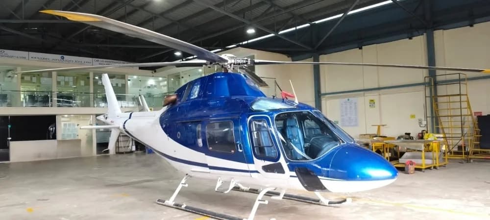 Front-side view of a blue and white helicopter with its main rotor blades extended, parked inside a hangar.