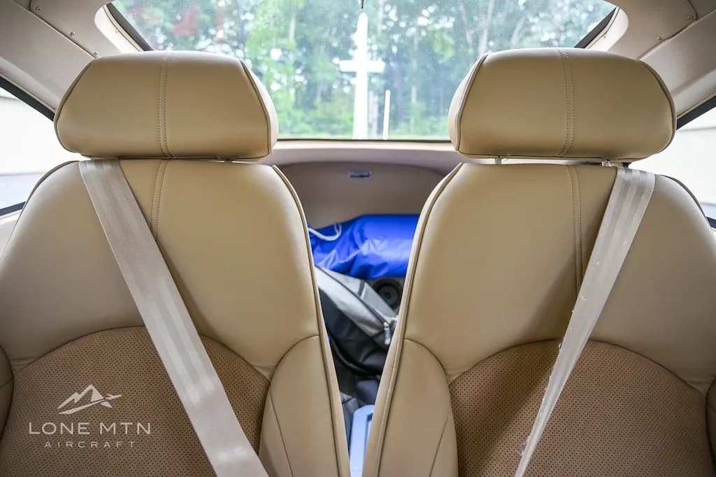 A view from the rear seats looking forward into the cabin of the aircraft, showing two tan leather seats with seatbelts.