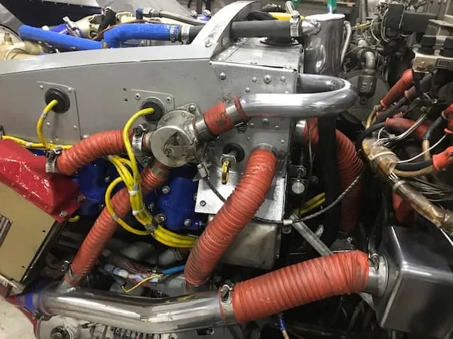A close-up view of an aircraft engine's components, showing red and blue hoses and metal parts.