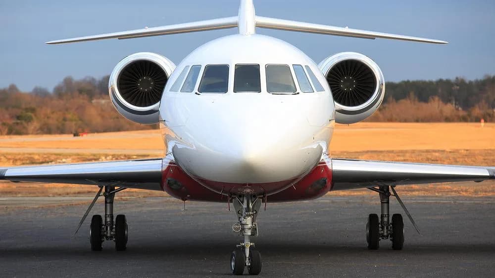A head-on view of a white and red Dassault Falcon 900 private jet on an airport tarmac.