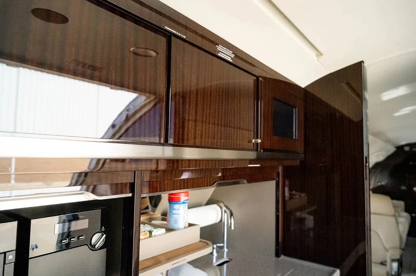 The galley area of a business jet, featuring dark wood cabinets, a microwave, and a sink.