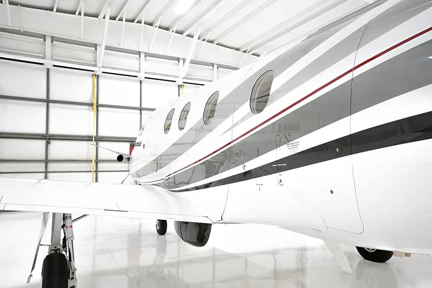 A close-up side view of the fuselage and wing of a white Pilatus PC-12 aircraft with gray and red stripes.