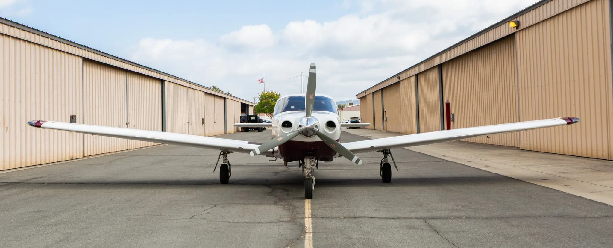 Frontal view of a white and maroon Piper Saratoga II TC aircraft, registration N691MA, parked on an asphalt ramp between hangars.