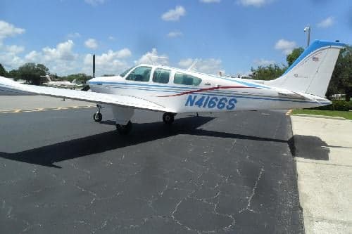 A Beechcraft Bonanza N4166S with blue and red stripes parked on the tarmac.