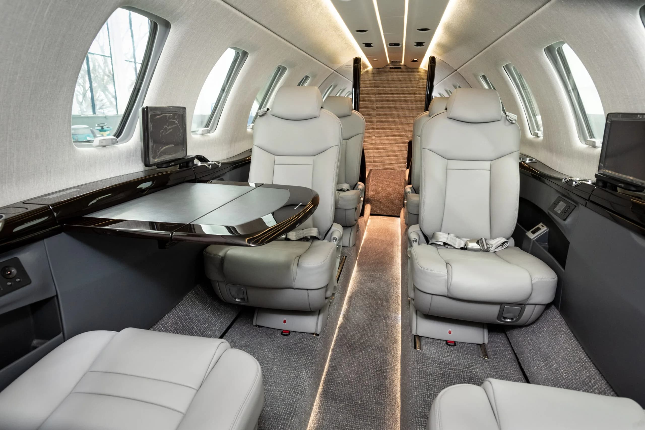 The luxurious interior cabin of a private jet with light gray leather seats and a fold-out table.