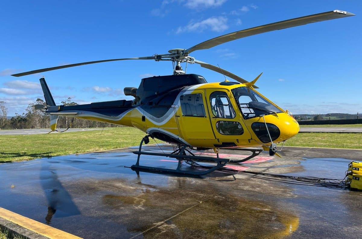 A yellow and black helicopter sits on a tarmac under a blue sky.