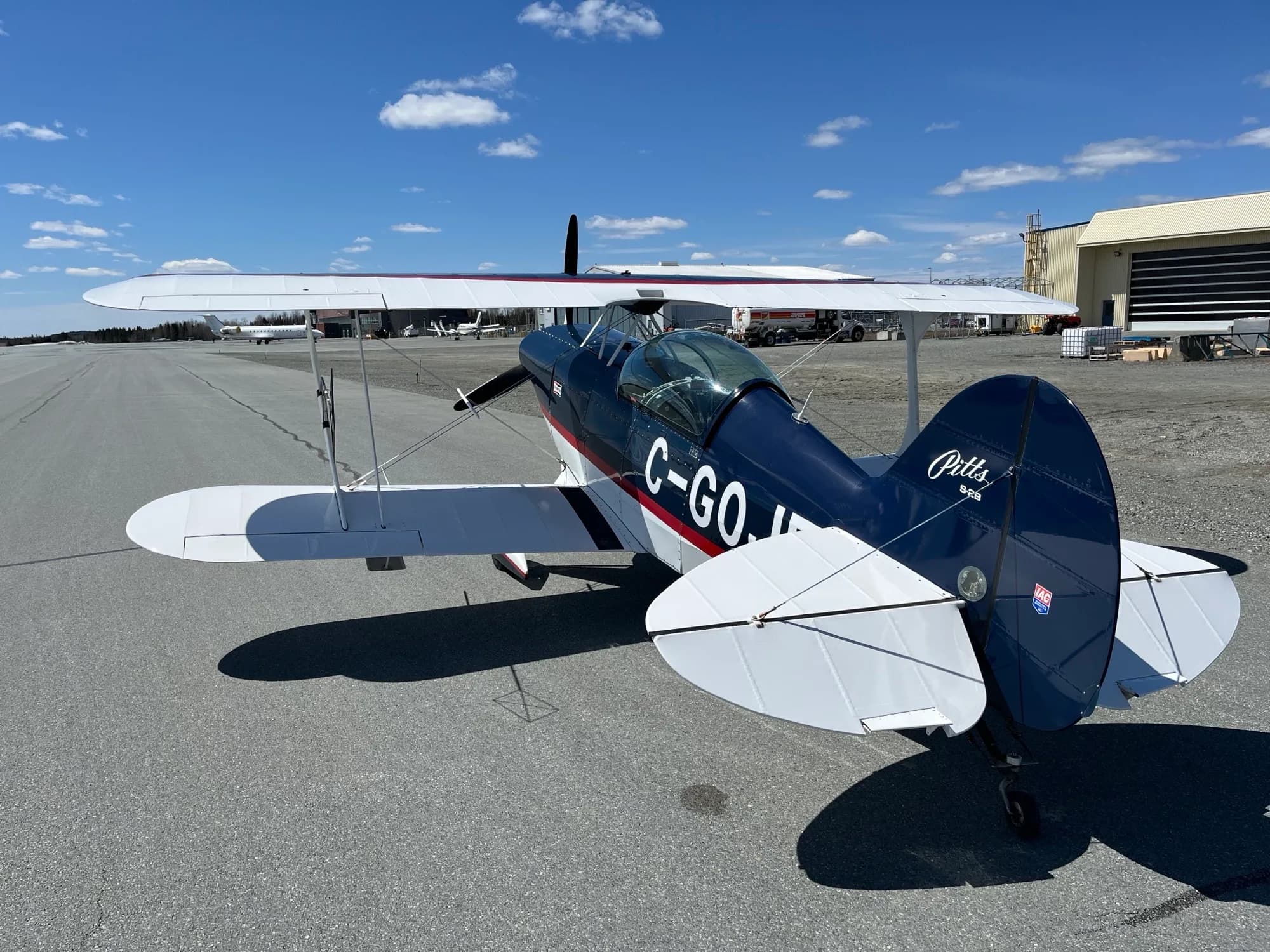 A rear-quarter view of the dark blue and white Pitts biplane C-GOJF parked on an asphalt runway.