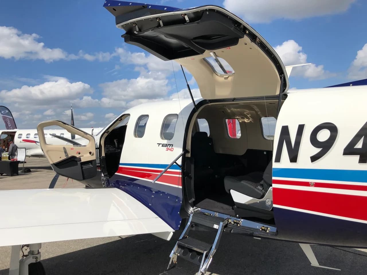 A TBM 940 aircraft with registration N940DF, showing the open main cabin door and steps on an airfield.