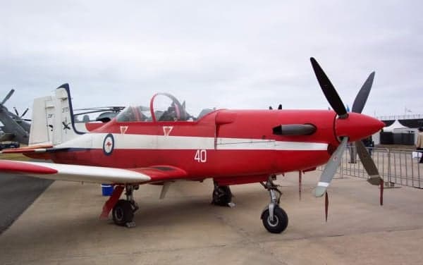 Front side view of a red and white Pilatus PC-9 aircraft on the ground.