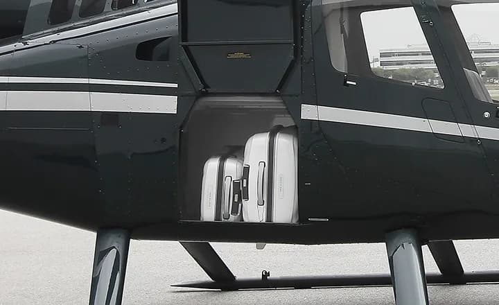 The luggage compartment of a dark green Robinson R66 Turbine helicopter with two white suitcases inside.