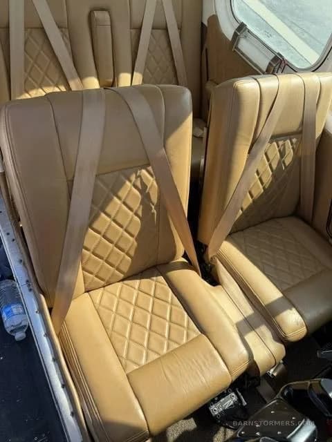 An interior view of an aircraft cabin featuring tan leather seats with diamond stitching and seatbelts.