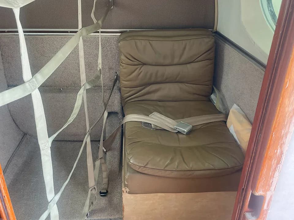 A single tan leather seat with a seatbelt in the aircraft cabin, next to a cargo net.