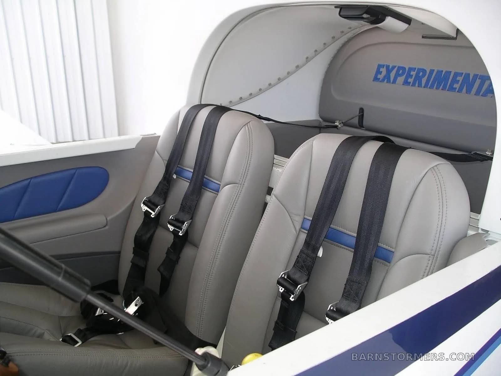 The interior of the aircraft features two gray leather seats with blue accents and black harnesses, and the word "EXPERIMENTAL" stenciled on the bulkhead.