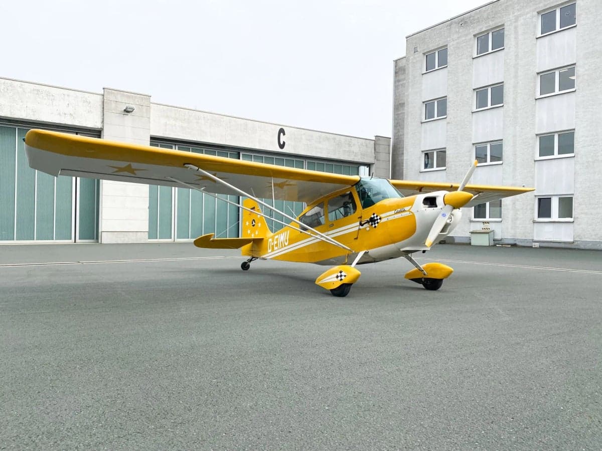 A yellow and white aircraft, D-EIMU, parked on the tarmac in front of a hangar.