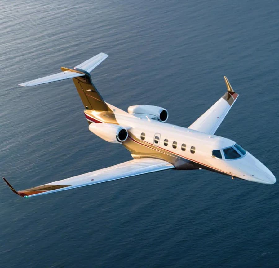 A white and gold jet flying over the ocean.