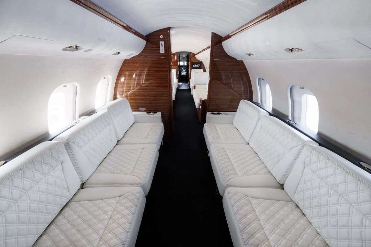 Interior view of a private jet cabin with white leather seats and dark wood trim.