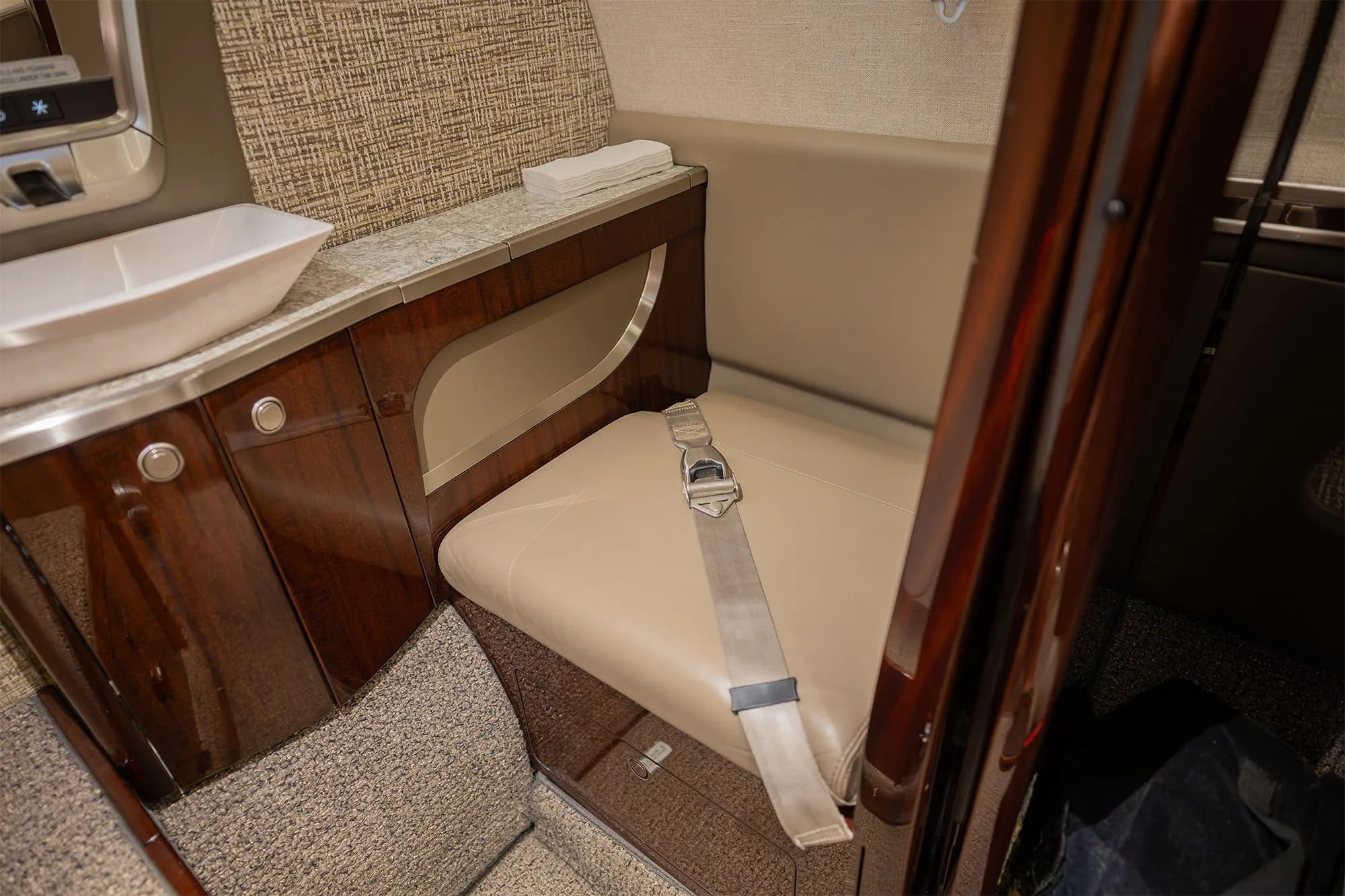 A close-up of a beige leather seat and a small counter with a sink in the cabin of a business jet.