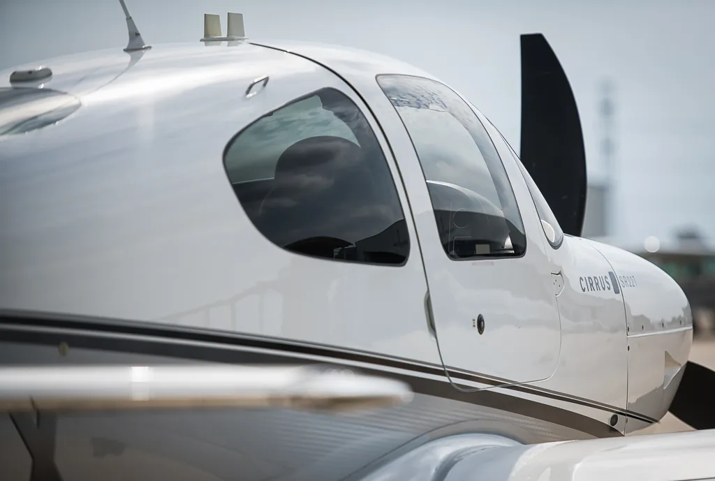 A close-up view of the cockpit and front fuselage of a white and silver Cirrus SR22T aircraft.