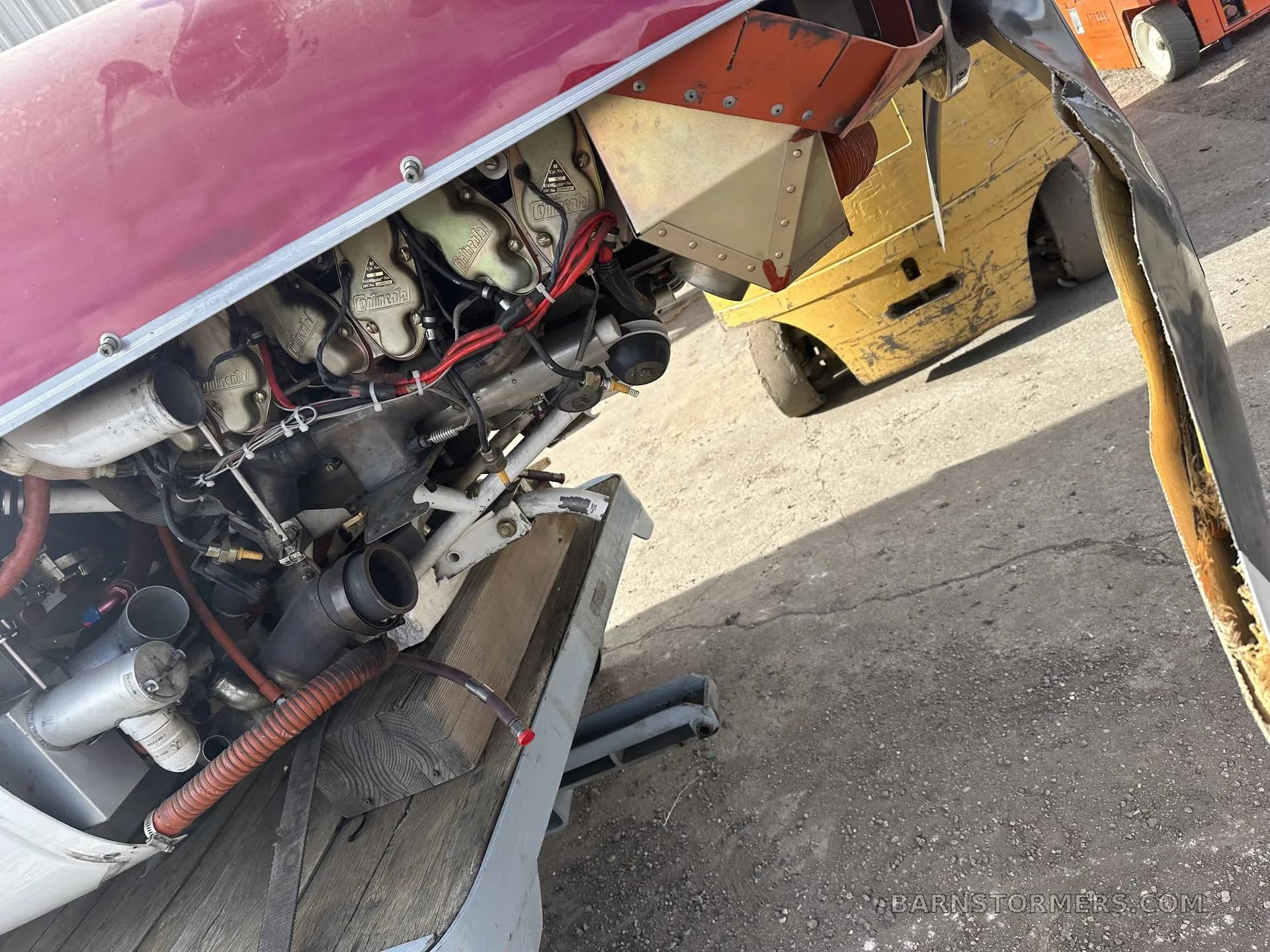 A close-up view of the exposed engine of a red aircraft, showing cylinders and exhaust pipes.