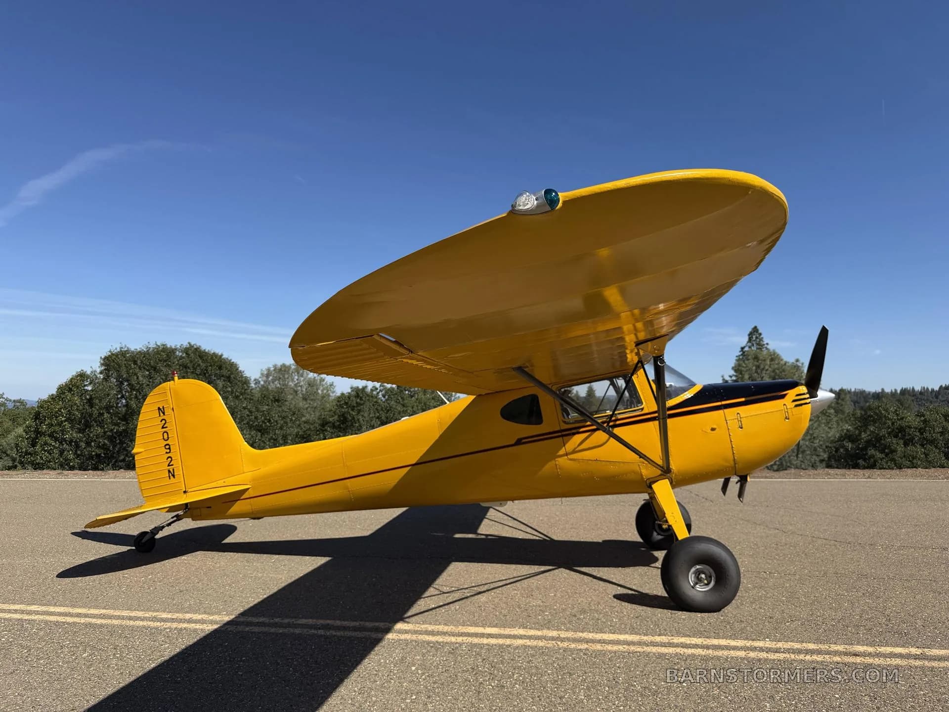 A bright yellow high-wing monoplane aircraft, N2092N, is parked on an asphalt surface under a clear blue sky, viewed from the front-right side.