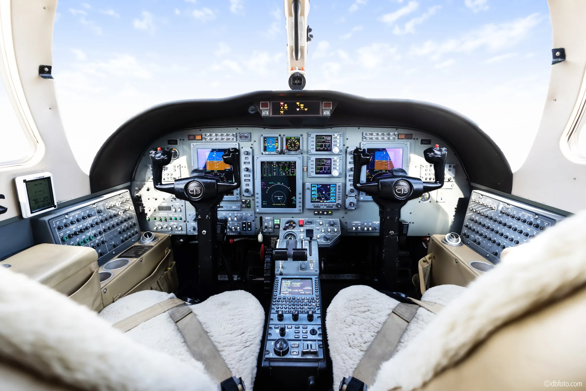 The cockpit of a Cessna Citation CJ3 business jet, showing the instrument panel, controls, and sheepskin-covered pilot seats.