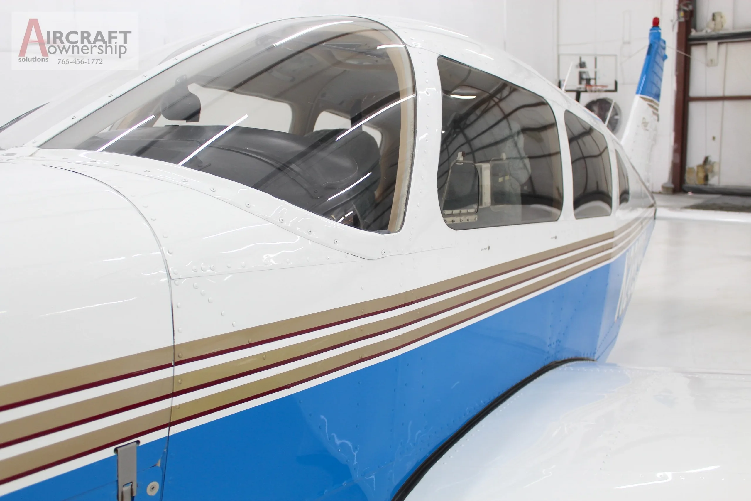 A close-up view of the cockpit and fuselage of a white and blue Piper Dakota aircraft.