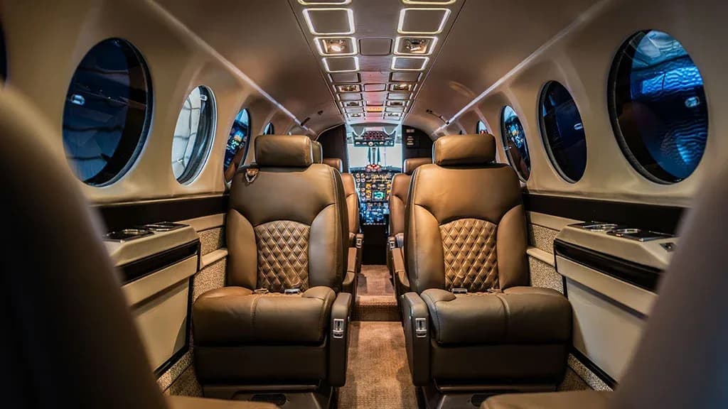 The luxurious interior cabin of an aircraft, featuring brown quilted leather seats and a view into the cockpit.
