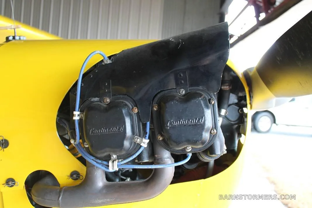 A detailed view of the Continental engine's exposed cylinders and blue ignition wires on a yellow aircraft.