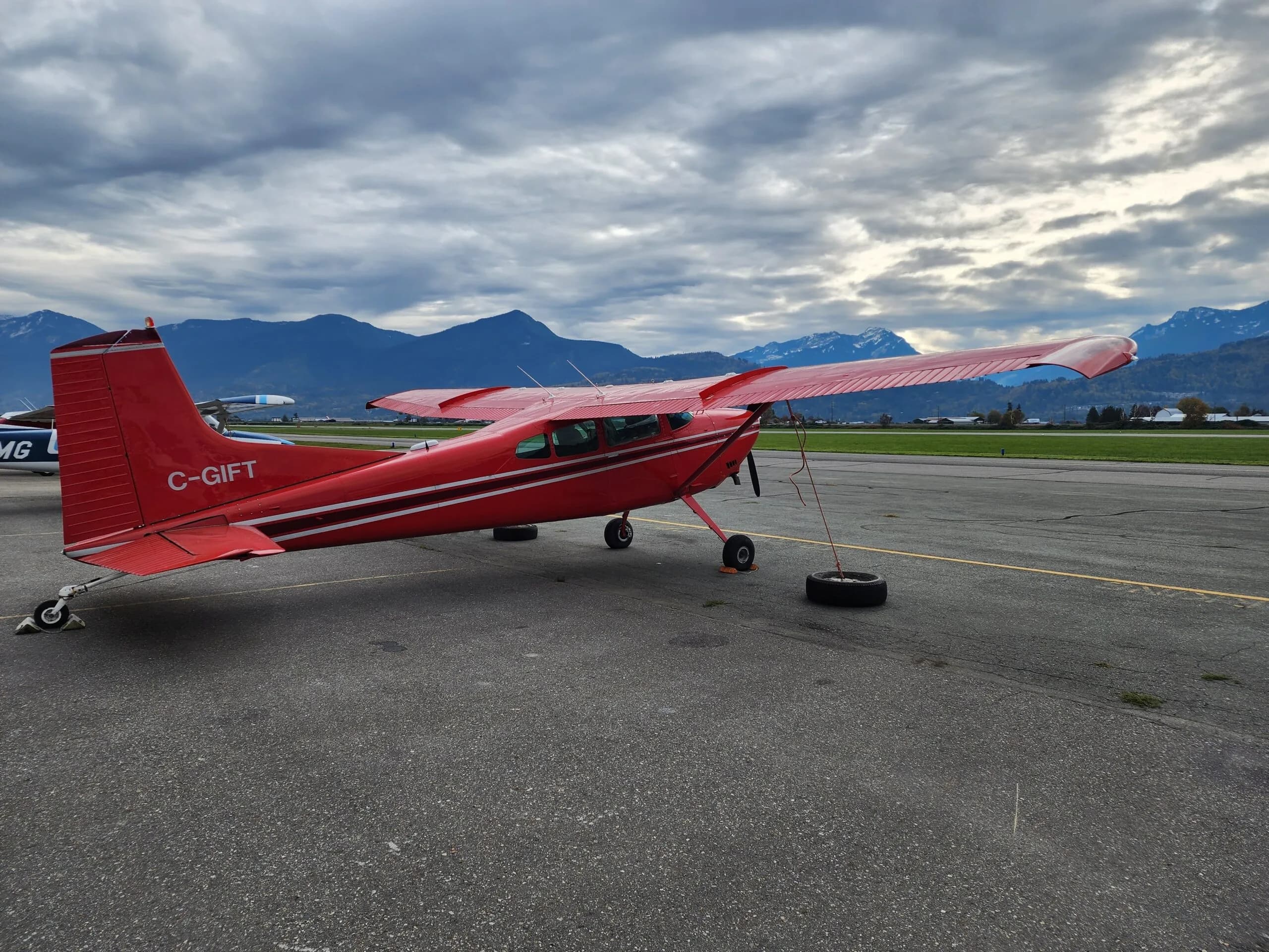 A red and white Cessna aircraft with registration C-GIFT parked on the tarmac with mountains in the background.