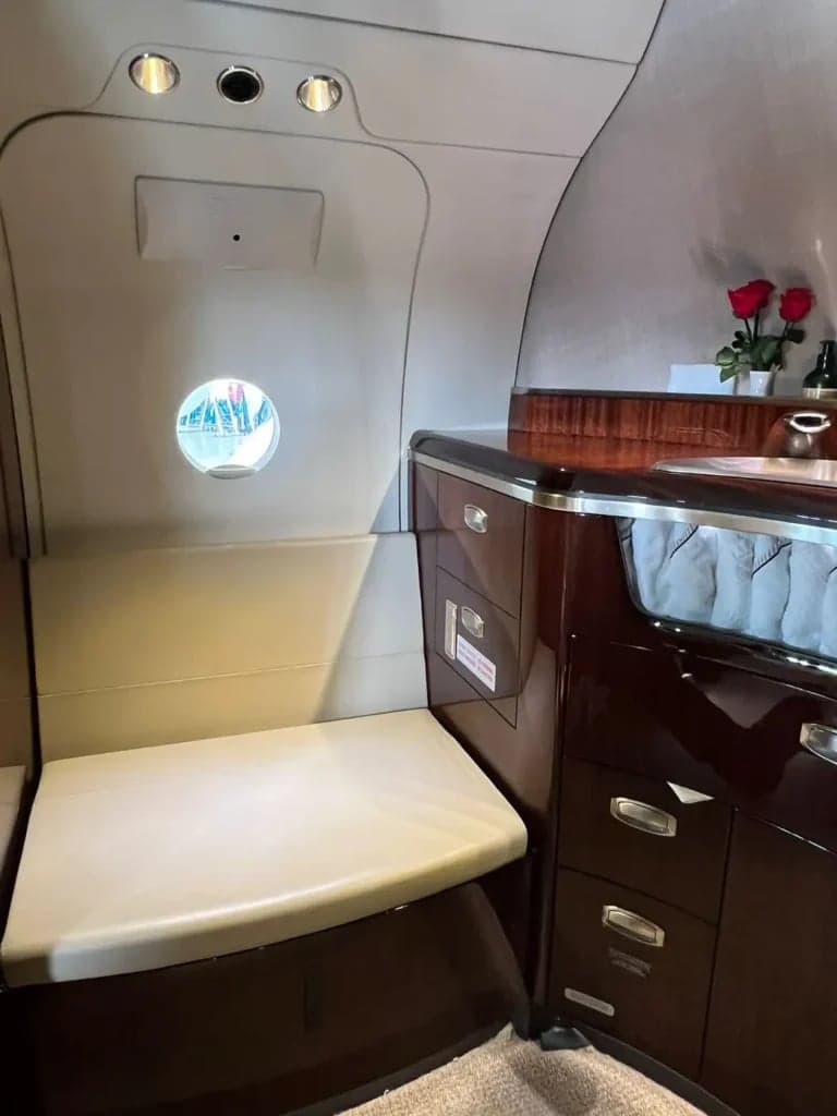 A view of the side of the aircraft cabin, showing a seat, storage, and a small window.