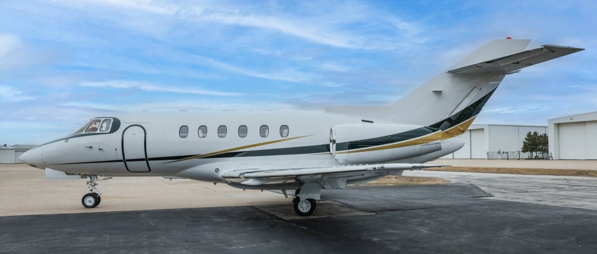 Side view of a Hawker 800XP with a white and gold paint scheme on the tarmac.