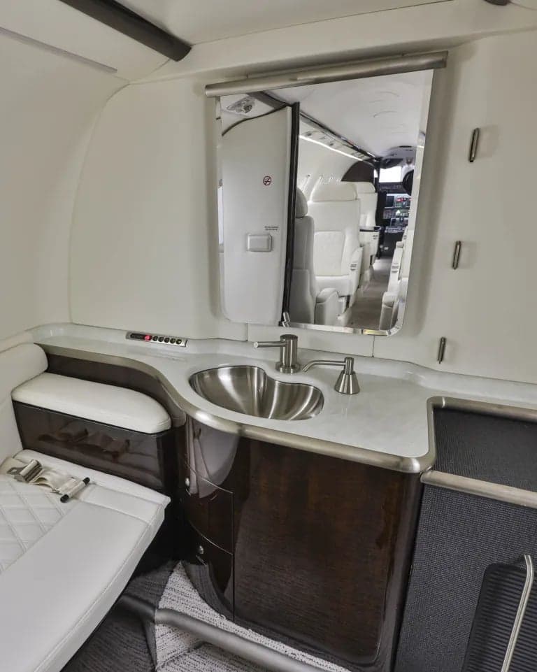 Aircraft lavatory with a sink, mirror, and white leather bench seat.