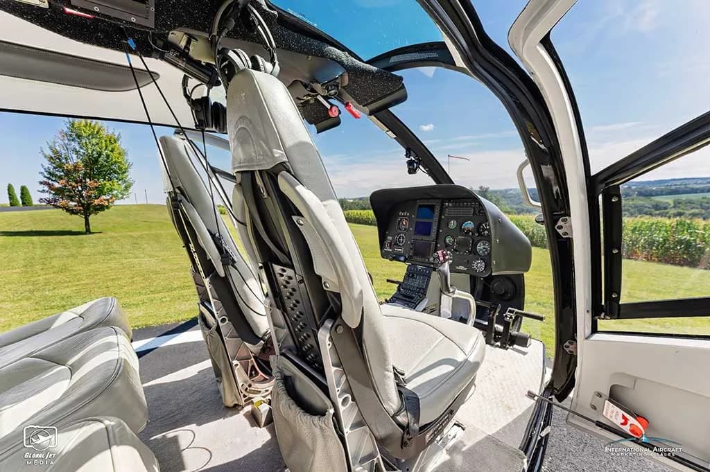 View from inside the helicopter cabin showing light grey pilot seats and a partial view of the cockpit.