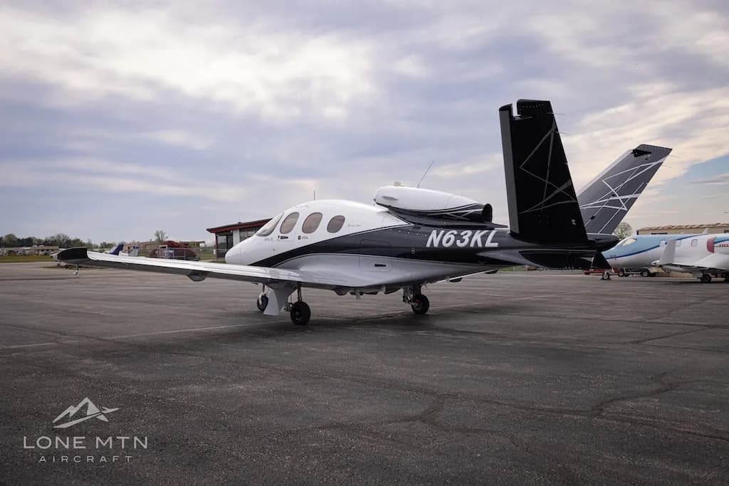 A rear three-quarter view of a white and black Cirrus Vision Jet (N63KL) parked on an asphalt apron.