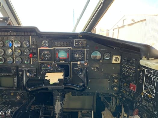 A close-up view of an aircraft's instrument panel, showing various gauges, screens, and the pilot's yoke.