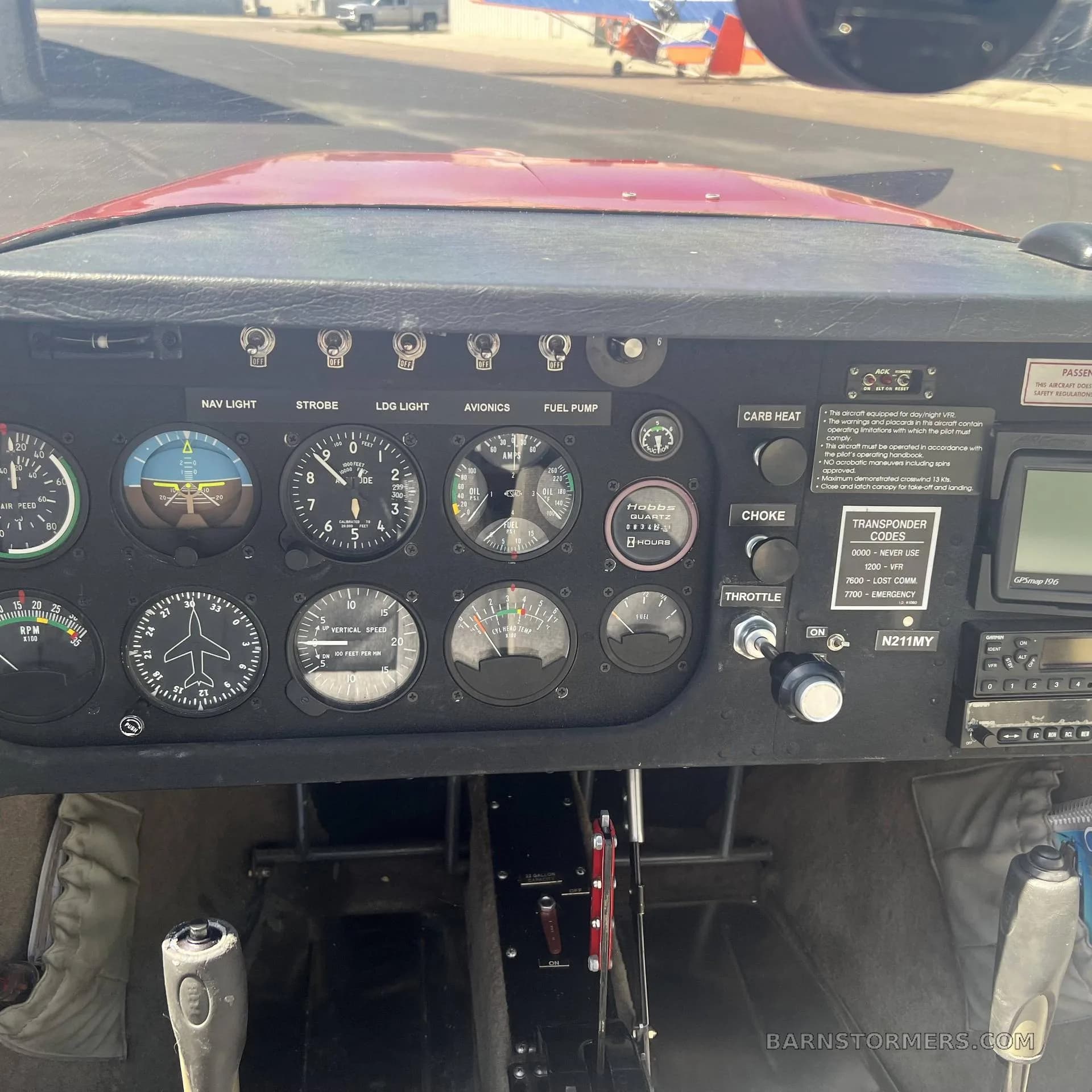 The cockpit instrument panel of a red Thorp T211 Torpedo aircraft, showing various gauges, switches, and a GPS unit.
