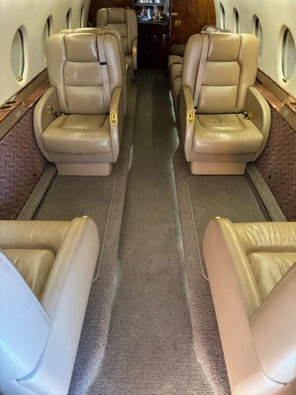 A view down the center aisle of the aircraft cabin, showing tan leather seating.