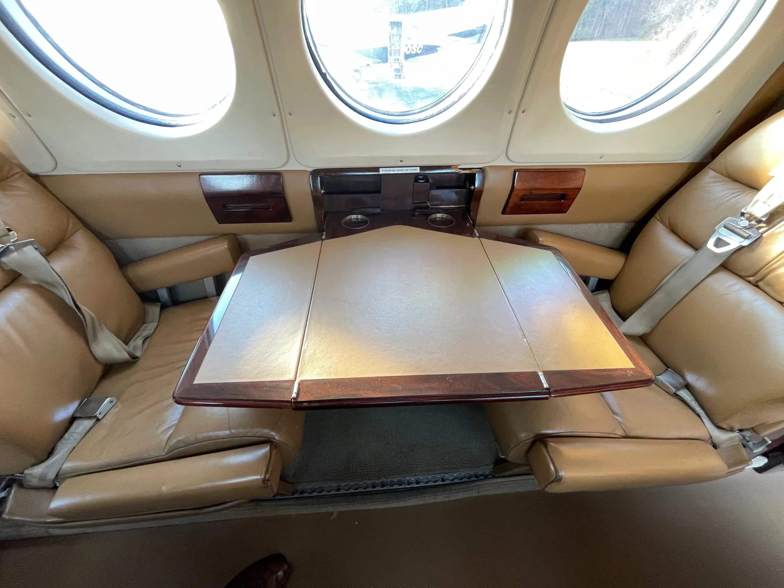 A fold-out table between two tan leather seats in the cabin of a private aircraft.