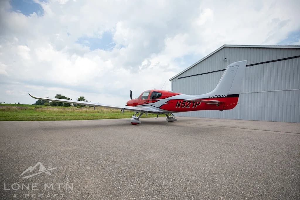 A red and silver Cirrus SR22 aircraft, N521P, seen from the rear-right, parked on an asphalt ramp.