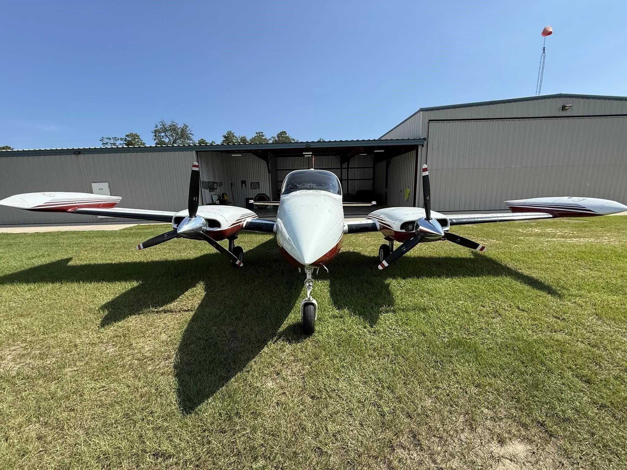 Head-on view of a white and red twin-engine aircraft (N310Z) parked on grass in front of a hangar.